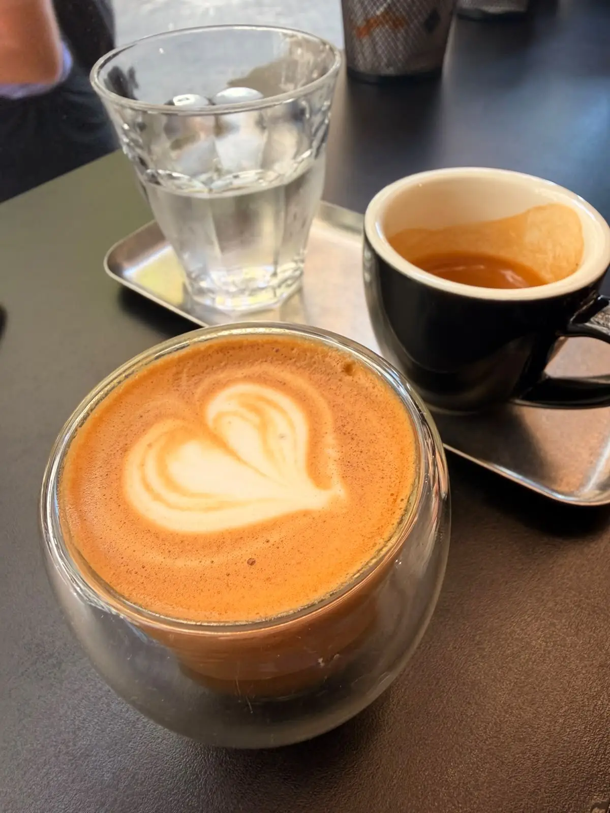 Un cortado con un corazón en la espuma y un espresso en taza negra